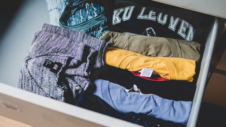 Tumpukan kaos berbagai warna terlipat rapi sebagai contoh pilihan warna seragam