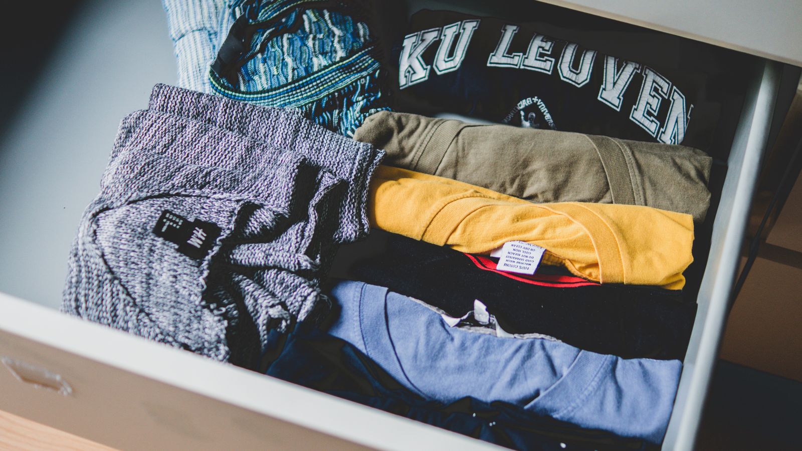 Tumpukan kaos berbagai warna terlipat rapi sebagai contoh pilihan warna seragam
